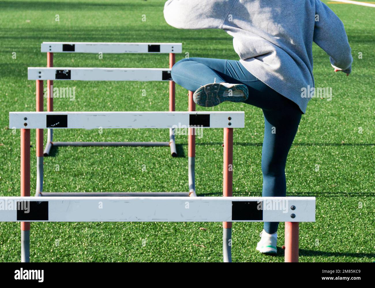 A high school girl is running a hurdle drill with her trail leg only