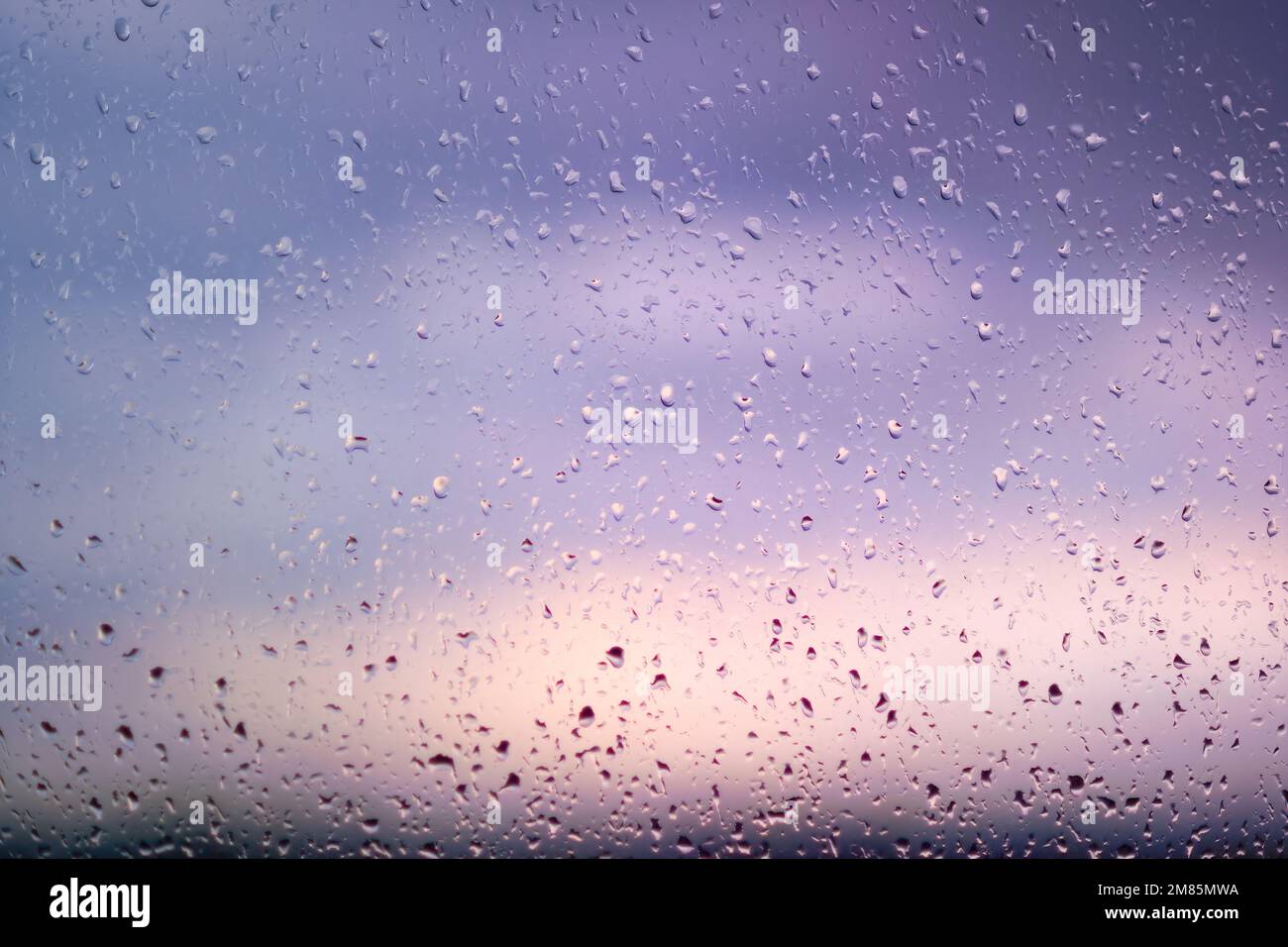 Natural water drops on a window agains a sunset sky. Stock Photo