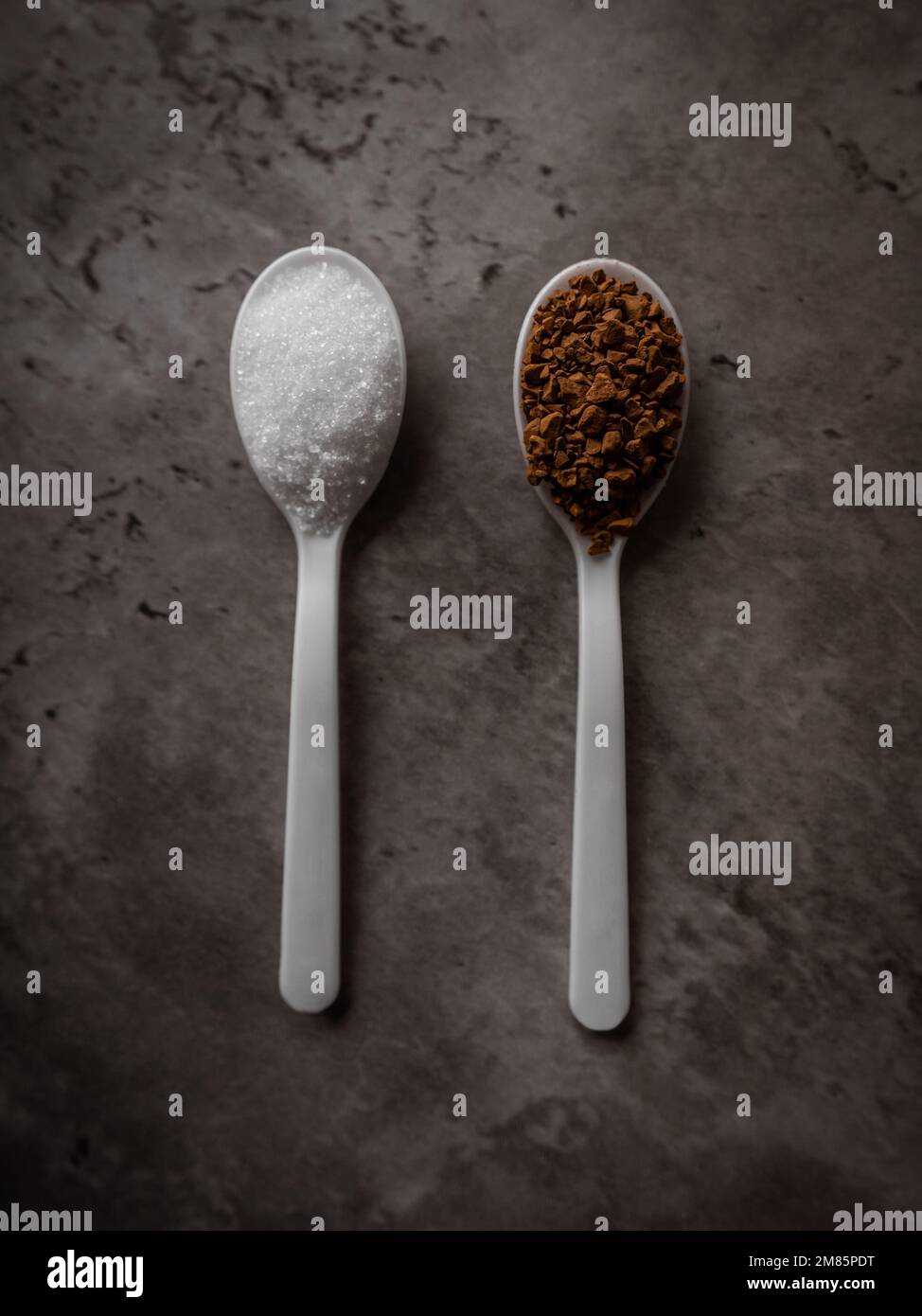 Two spoonfuls of instant coffee and sugar on the kitchen counter in equal portions. Top view flat lay with vertical orientation. Excess sugar concept Stock Photo
