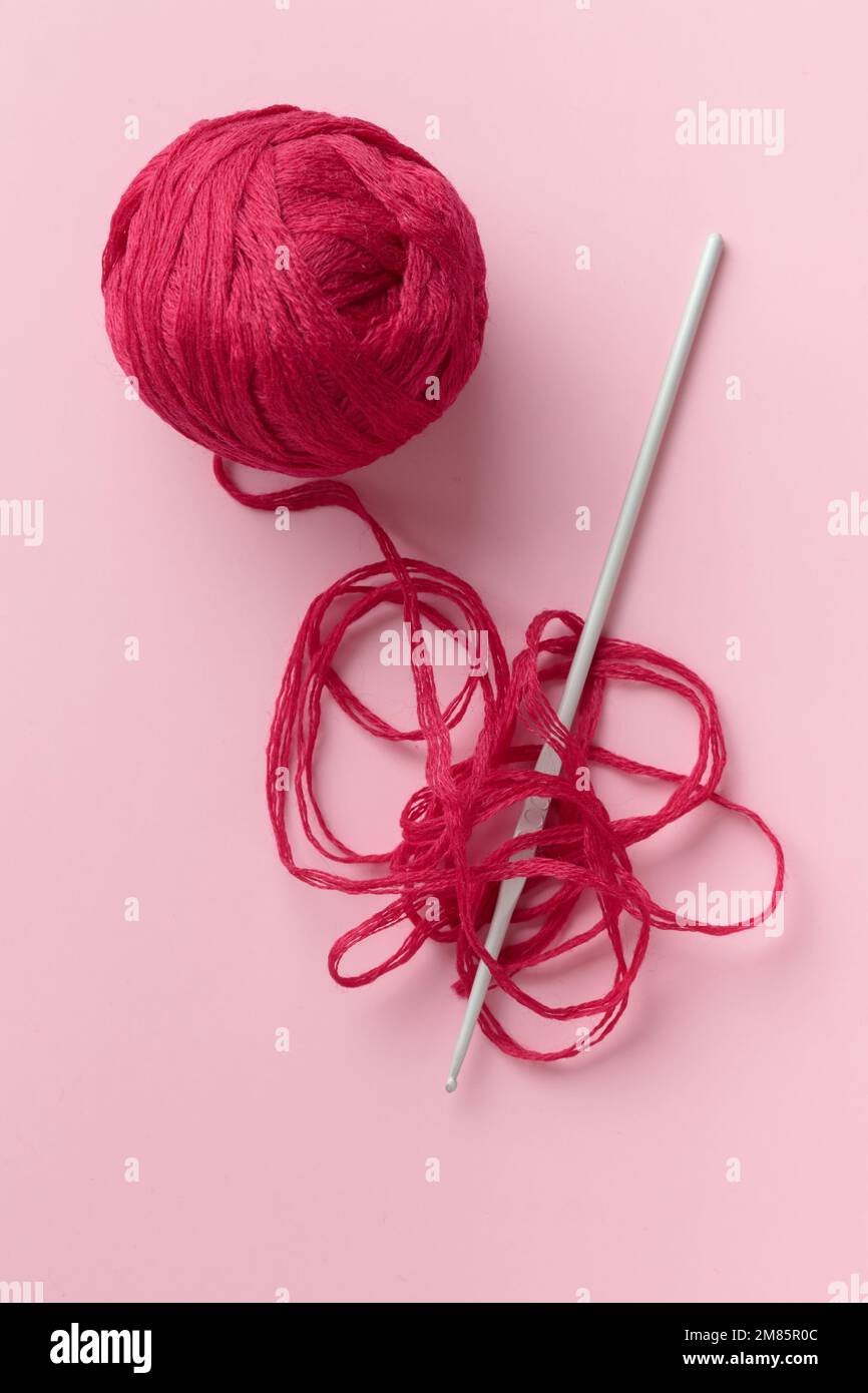 Crocheted hook and purple red burgundy skein of yarn with a crochet hook on a pink background with a copyspace Stock Photo