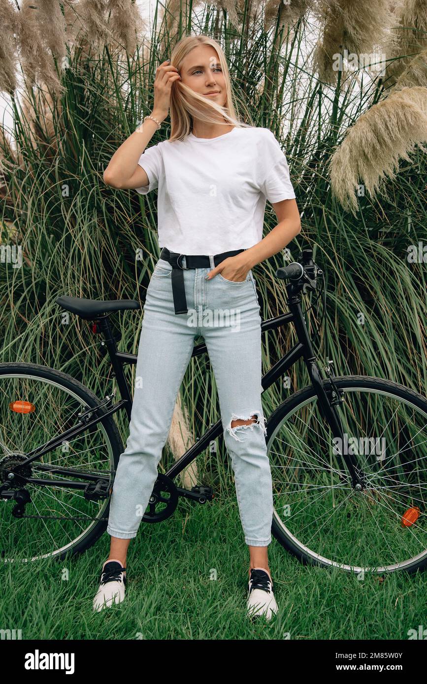Young beautiful girl is posing in a white t-shirt next to her bike. Vertical mockup. Stock Photo