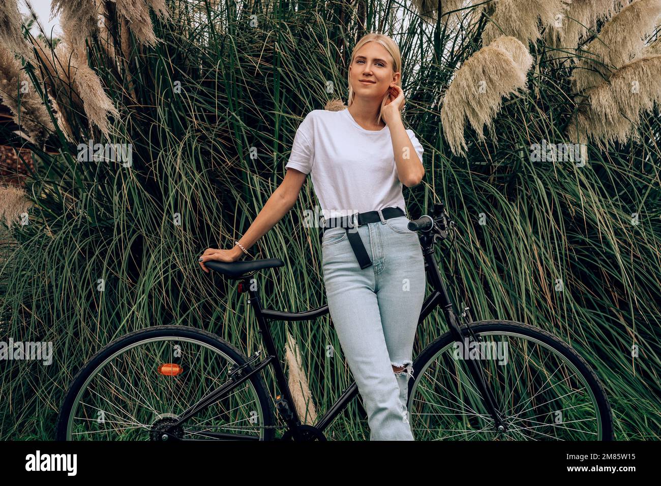 Young beautiful girl is posing in a white t-shirt next to her bike. Horizontal mockup. Stock Photo