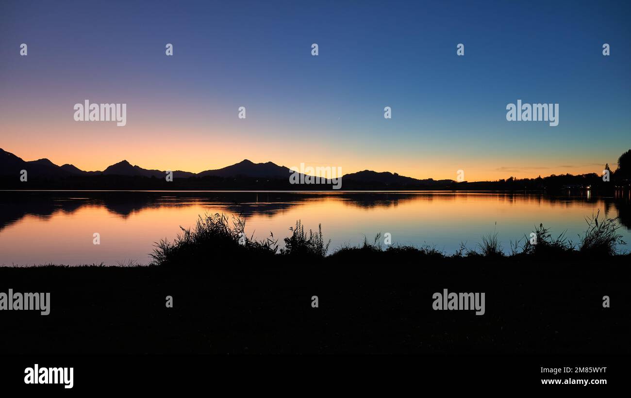 Hopfensee nach Sonnenuntergang mit wunderschöner Lichtreflexion und Bergsilhouette Stock Photo