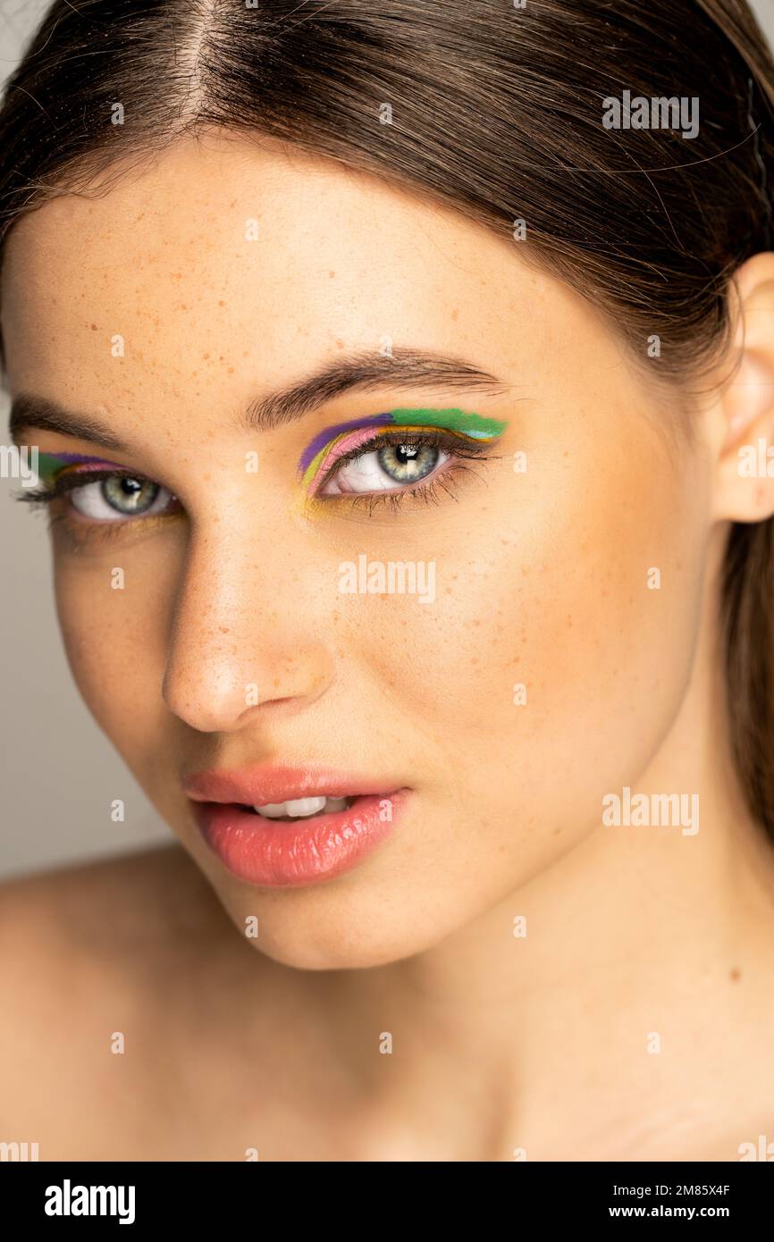 Teen model with colorful makeup and freckles looking at camera isolated on grey Stock Photo