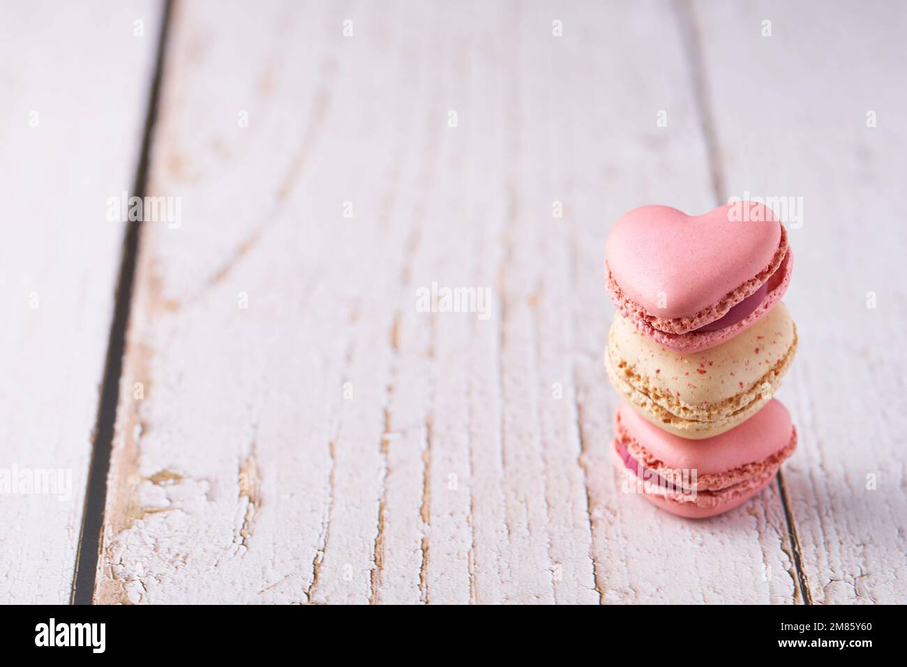 Stack of three heart shaped cream filled French macaroons on white wooden background. Confections for Valentine's Day, Mother's Day or Wedding. Stock Photo