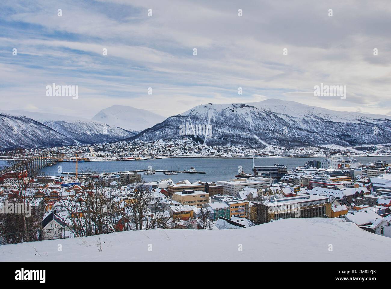 winter landscape of the port of Tromso in a fjord at the coastline of northern Norway with snow covered mountains in the background Stock Photo