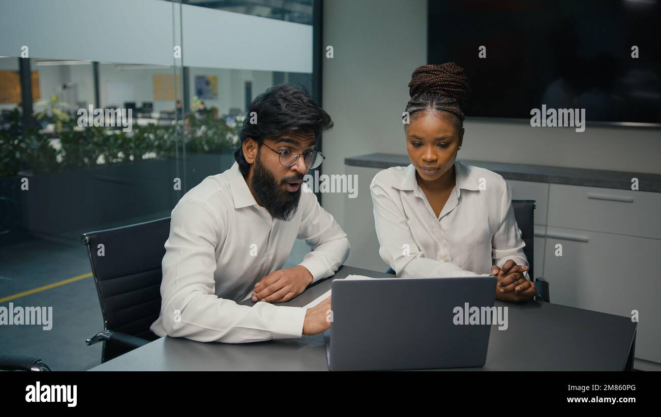 Business partners multiracial diverse company coworkers colleagues in office Indian man and African woman solving online problem with laptop computer Stock Photo