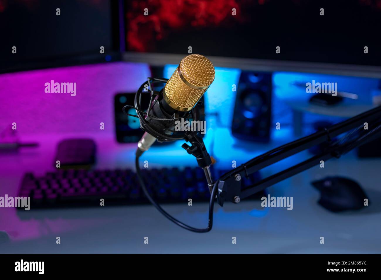 Condenser microphone in gamer setup with monitors, keyboard, mouse and colored lights. Stock Photo