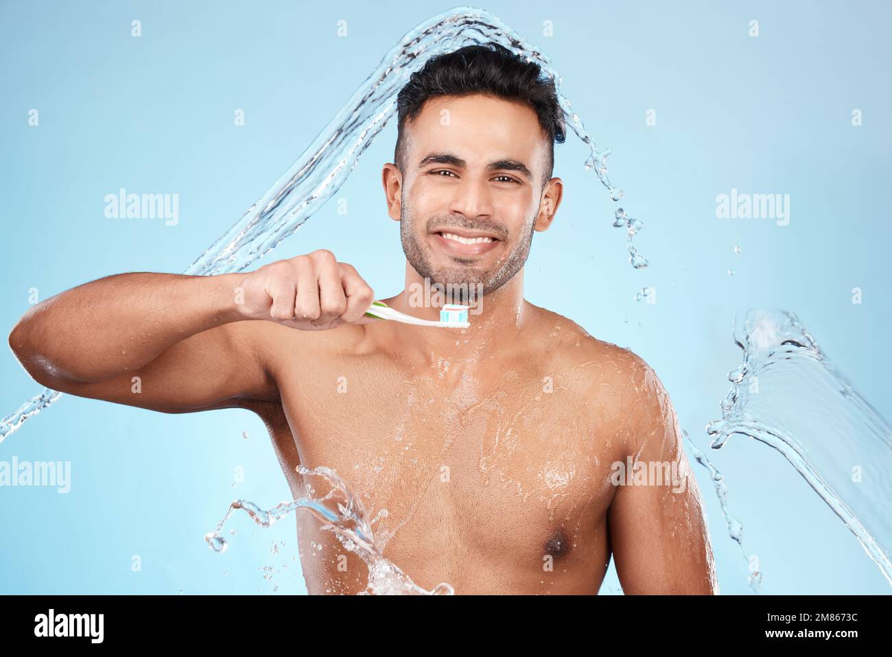 Face, water splash and man with toothbrush for cleaning in studio on blue background. Dental veneers, hygiene and portrait of happy male model Stock Photo