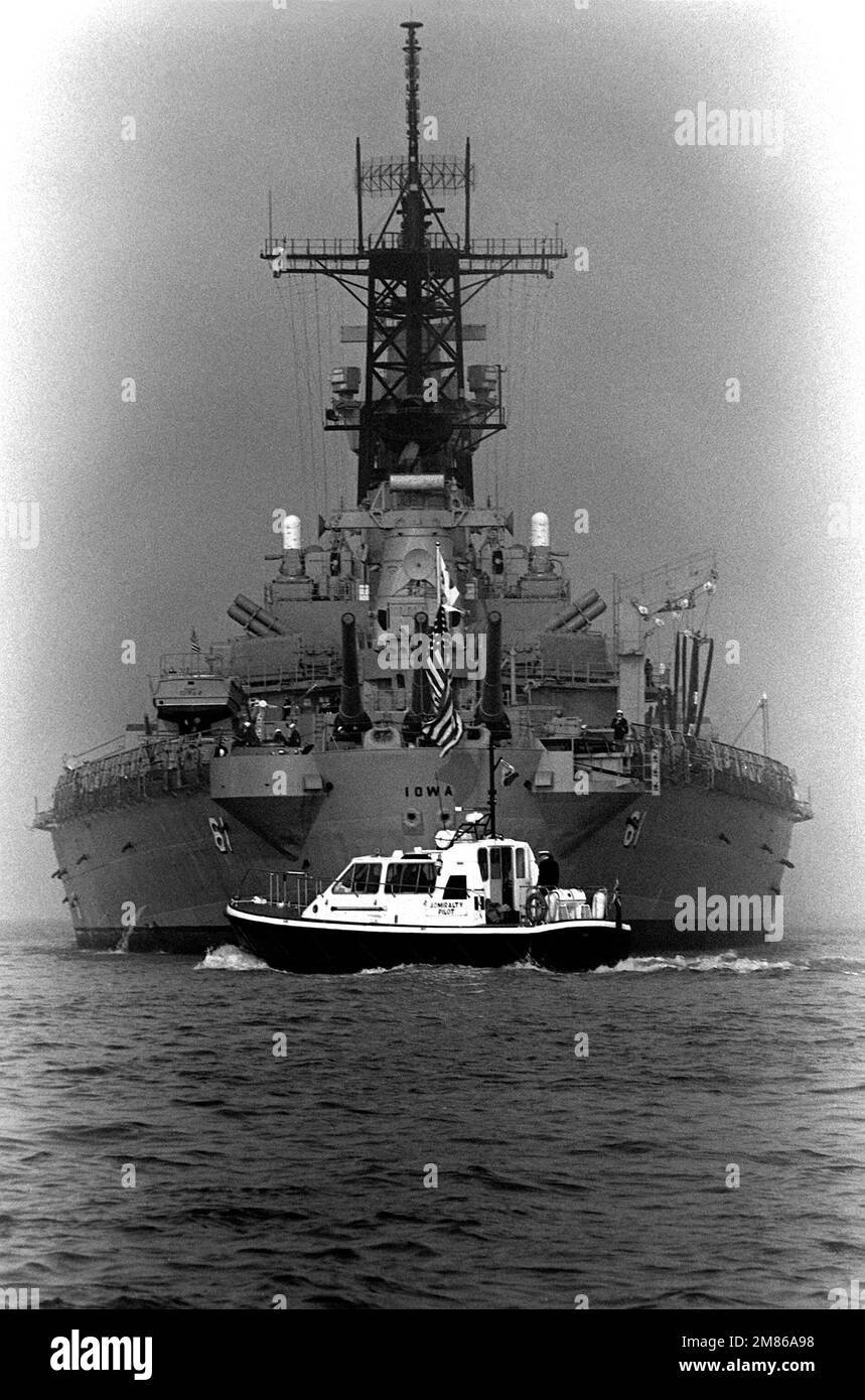 A small British pilot boat passes off the stern of the battleship USS