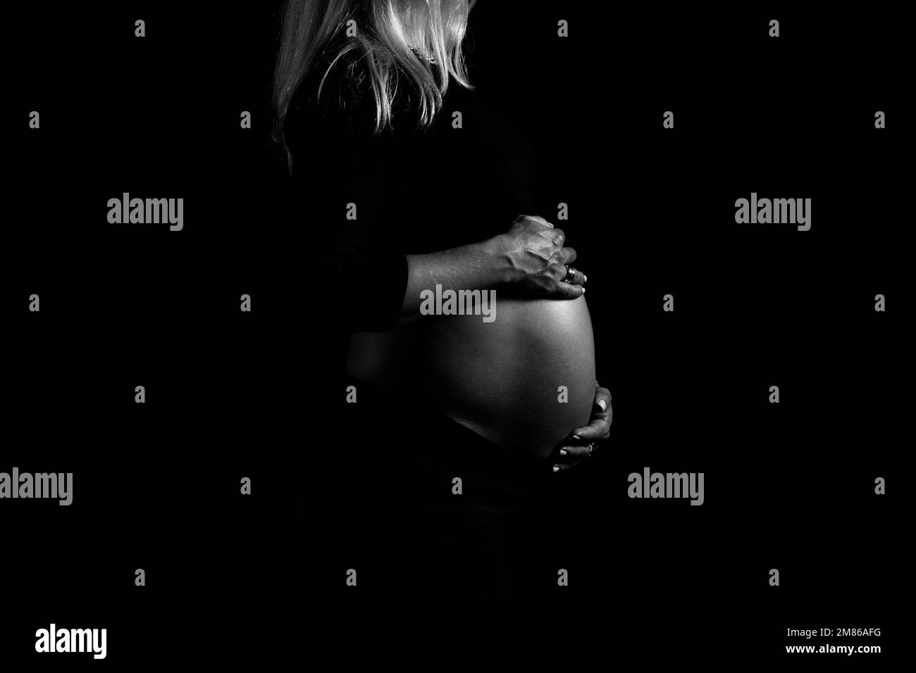Black and white view of pregnant woman gently holds her belly and caring about her health. Pregnancy, maternity, preparation and expectation concept. Stock Photo