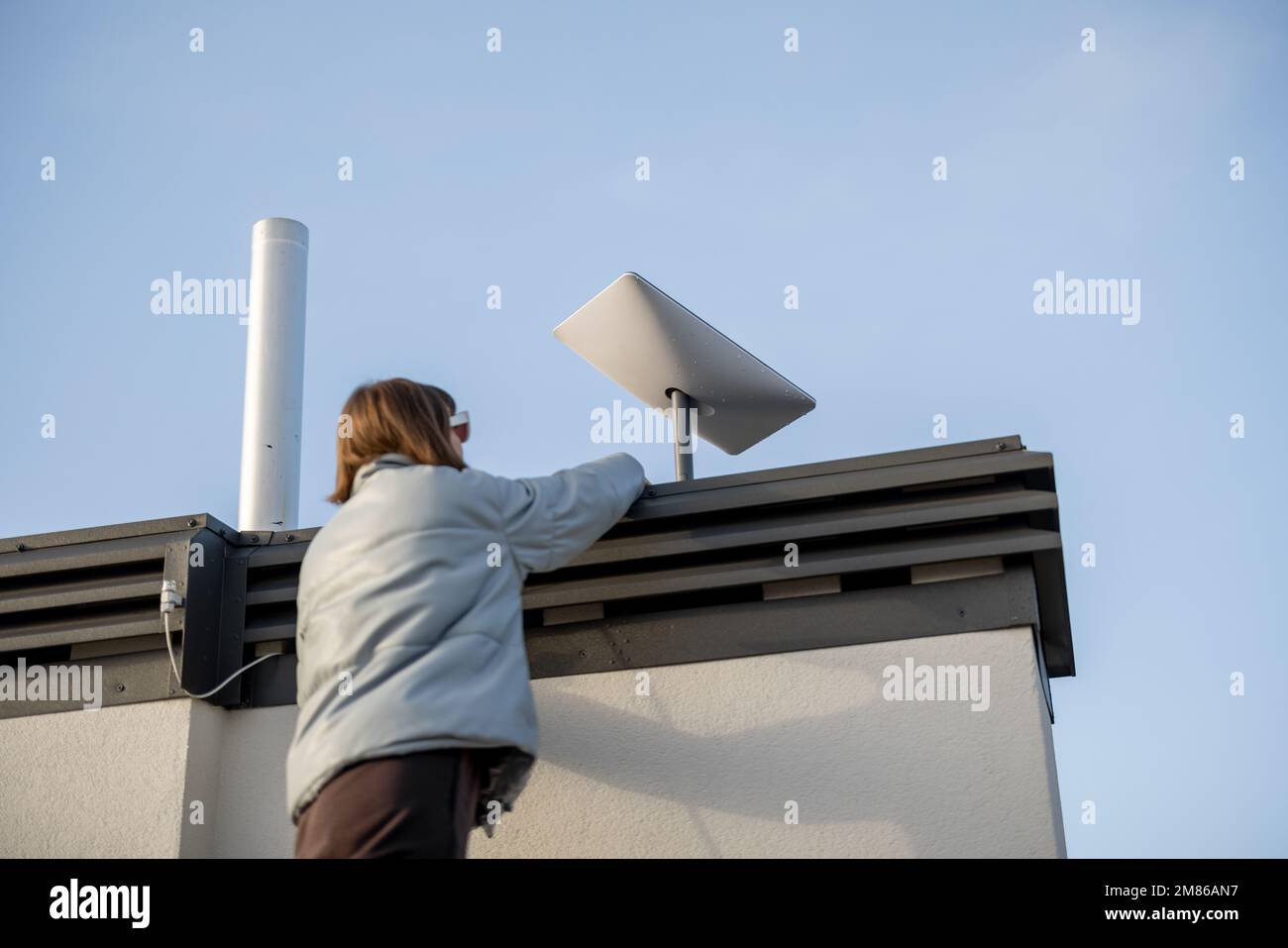 Woman installing Starlink satellite dish on roof of her house Stock