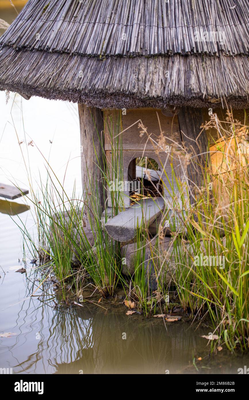 Wooden birdhouse on the water, roof made of straw. Stock Photo