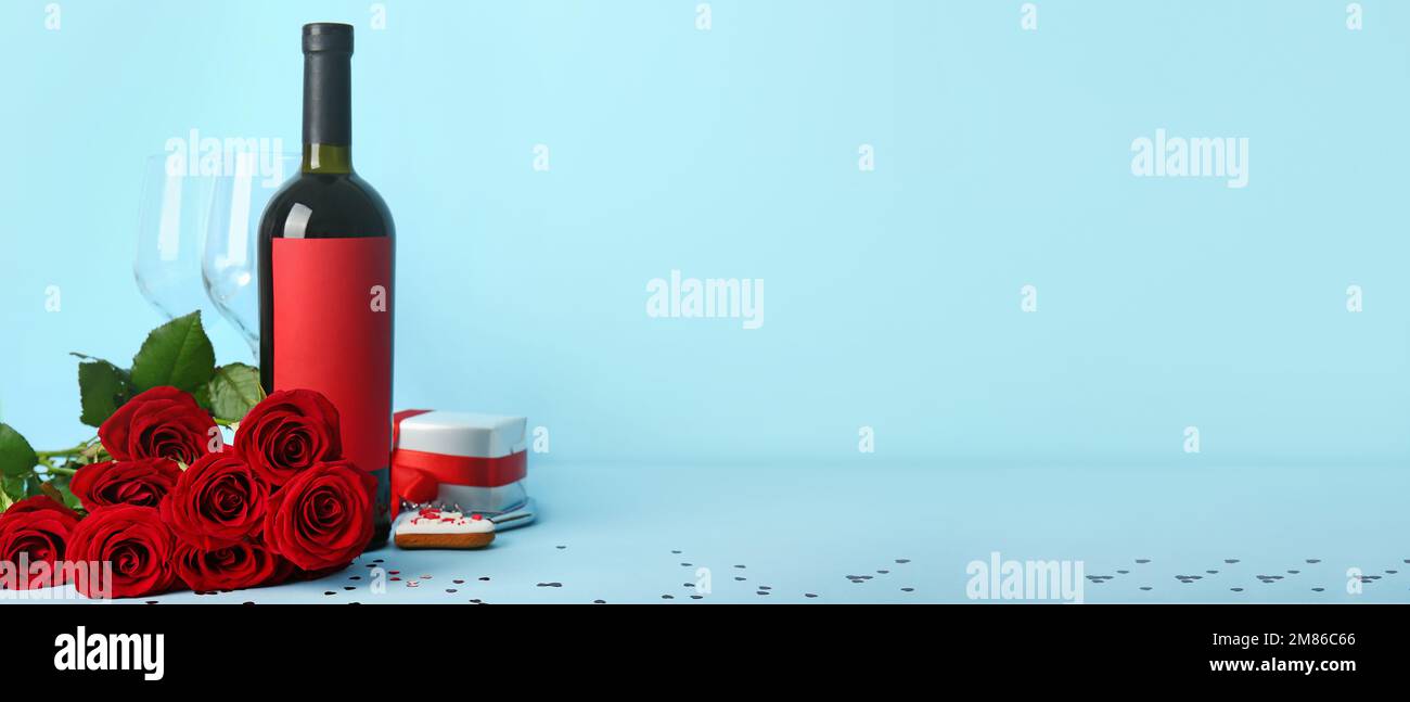 Bottle of wine, red rose flowers, glasses and gift on blue background ...