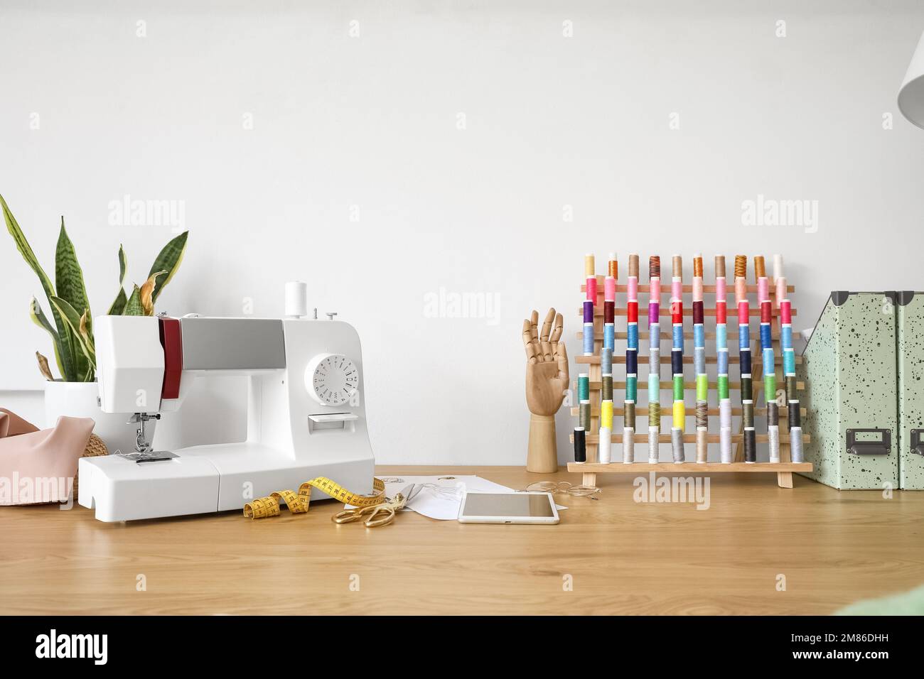 Tailor's workplace with sewing machine and thread pools near light wall ...