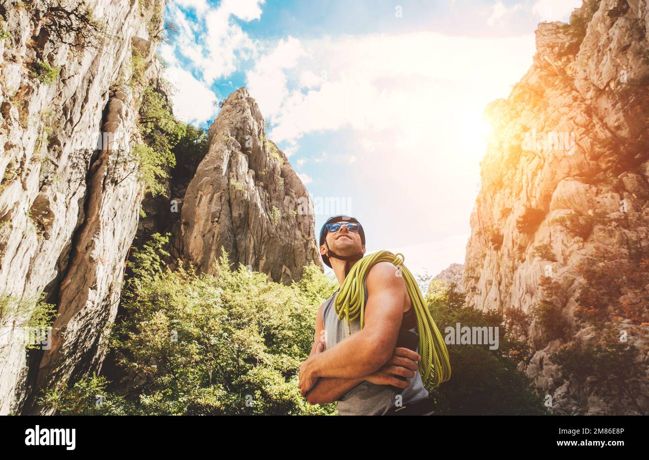 Smiling climber man in protective helmet and sunglasses with climbing rope on the shoulder in the Paklenica between rock cliff walls. Active extreme s Stock Photo