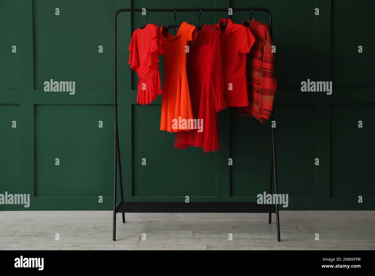 Rack with red female clothes near green wall Stock Photo - Alamy
