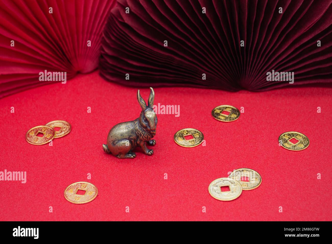 A bronze figure of a bunny hare with golden coins - the symbol of the Chinese new year 2023 on a red background, copy space. Stock Photo