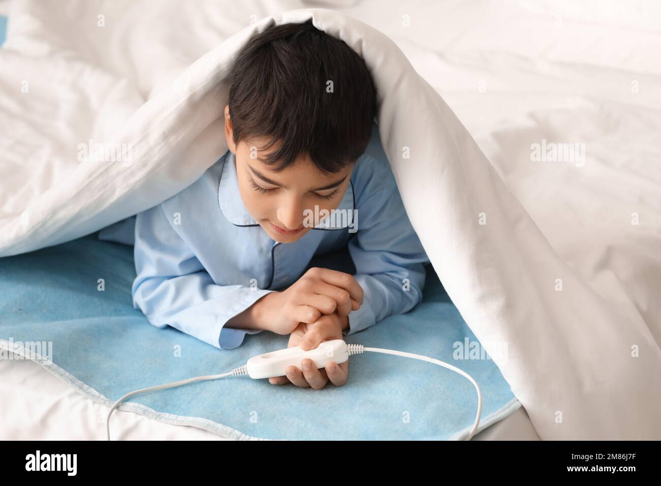 Little boy lying under blanket on electric heating pad in bedroom Stock
