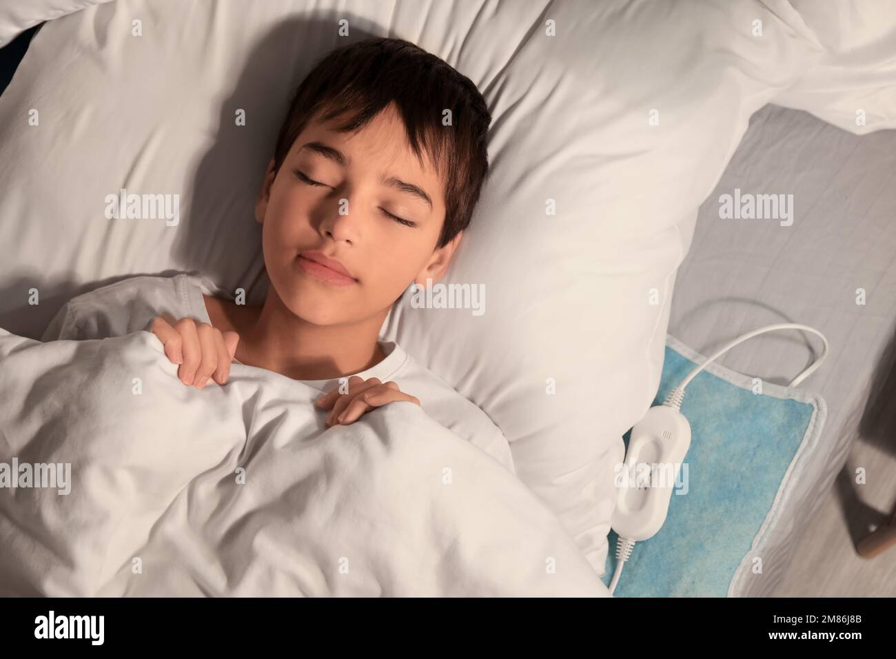 Little boy sleeping on electric heating pad in bedroom at night, top