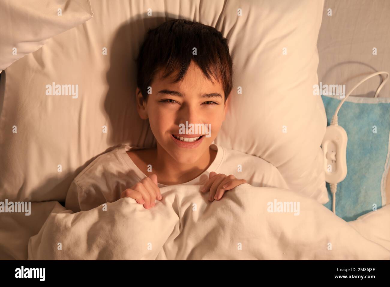 Little boy lying on electric heating pad in bedroom at night, top view