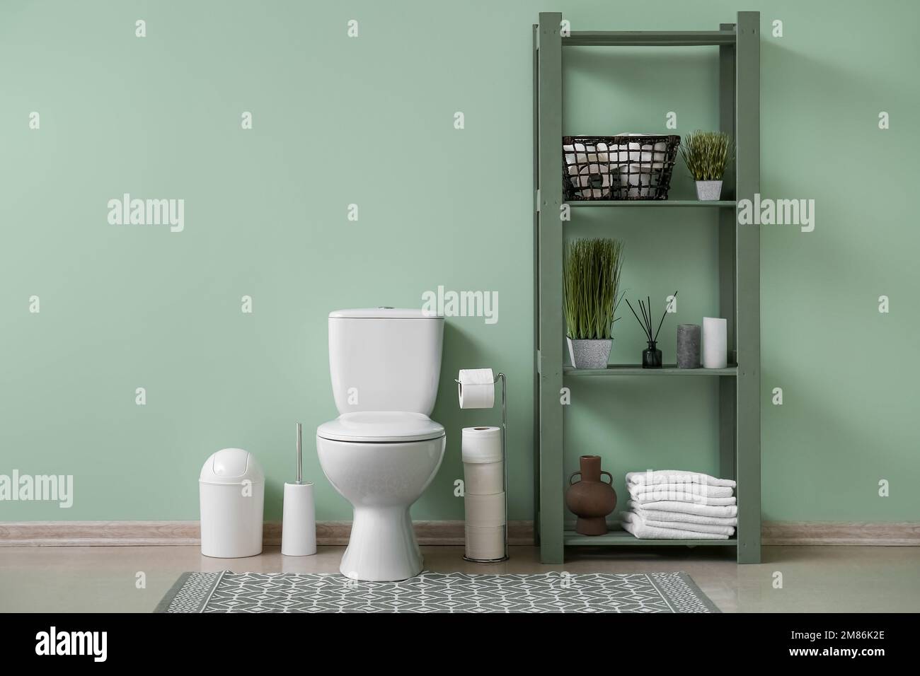 Interior of restroom with ceramic toilet bowl, rug and shelving unit ...