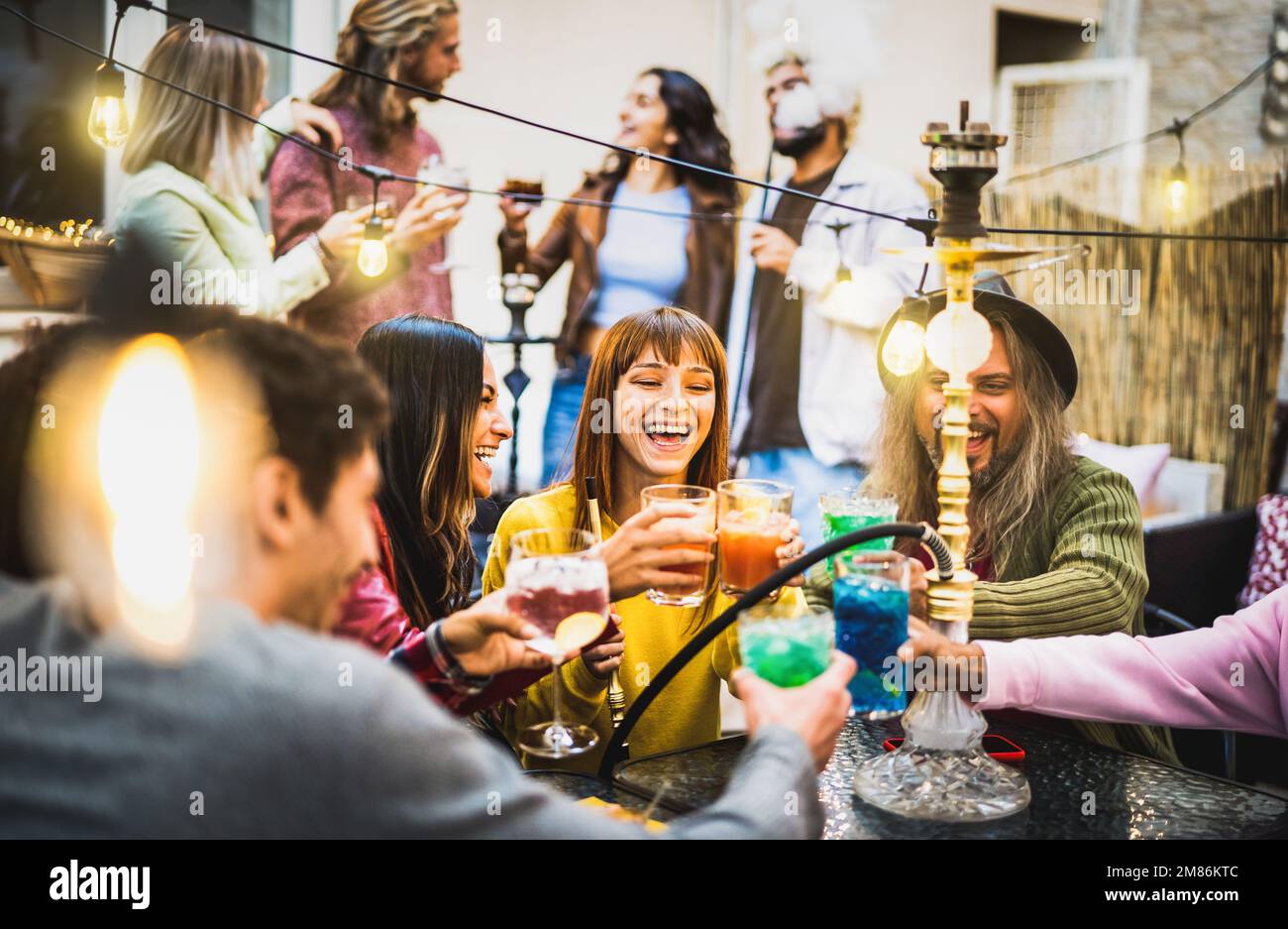 Trendy people having fun time enjoying cocktails at shisha bar - Mixed age range friends toasting drinks at fancy restaurant garden together - Food an Stock Photo