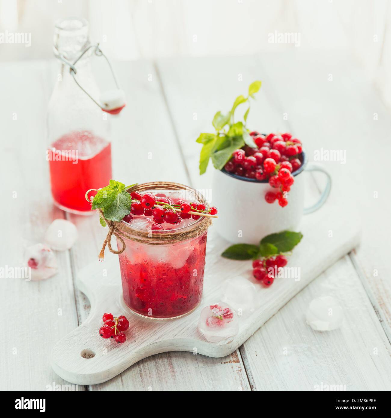 Summer drink with white sparkling wine. Homemade refreshing fruit cocktail or punch with champagne, red currant, ice cubes and mint leaves on white Stock Photo