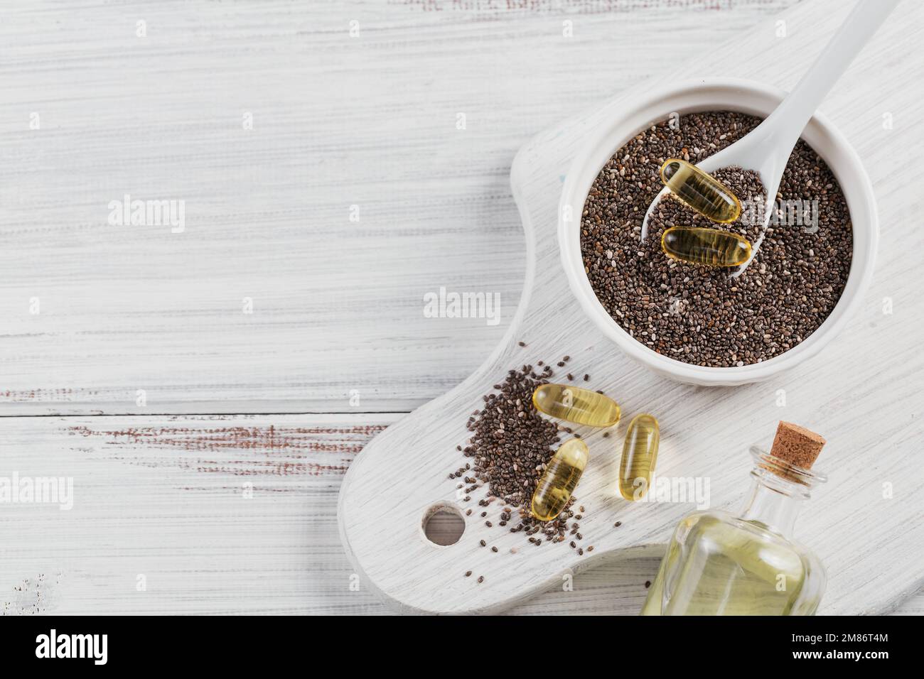 Chia seed in small bowl and gelatin capsules with omega oil on a white