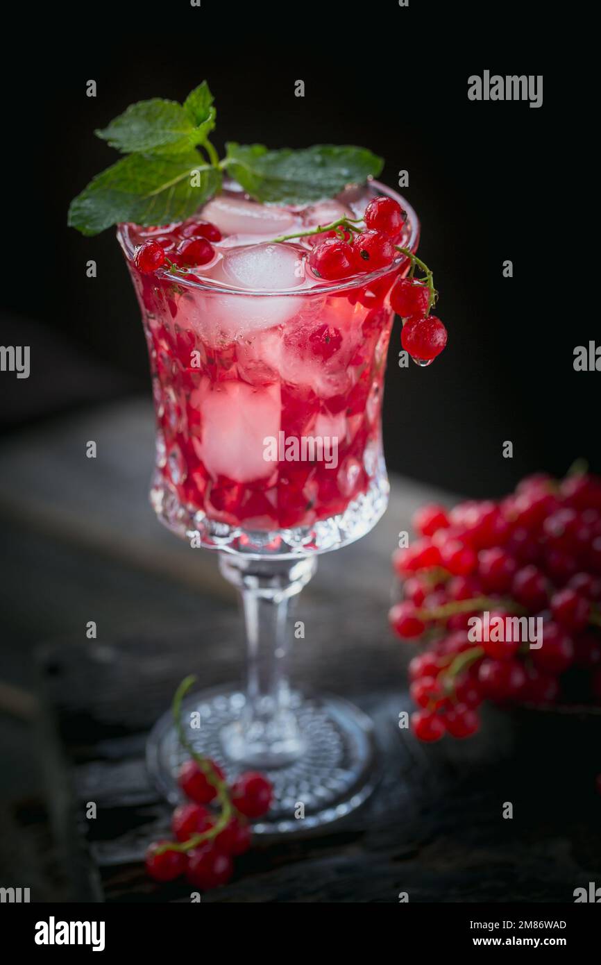 Summer drink with white sparkling wine. Homemade refreshing fruit cocktail or punch with champagne, red currant, ice cubes and mint leaves on a dark Stock Photo