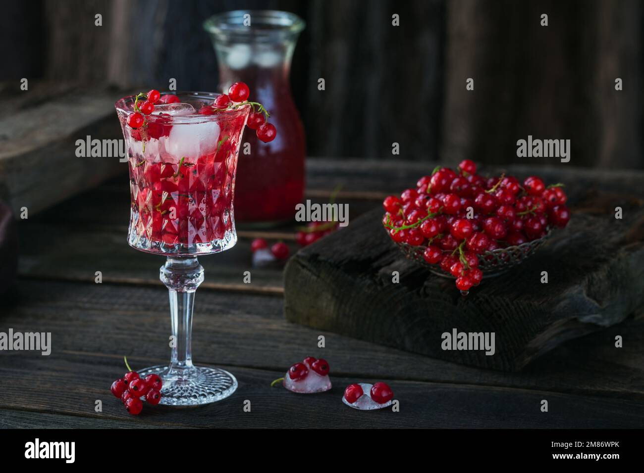 Summer drink with white sparkling wine. Homemade refreshing fruit cocktail or punch with champagne, red currant, ice cubes and mint leaves on a dark Stock Photo