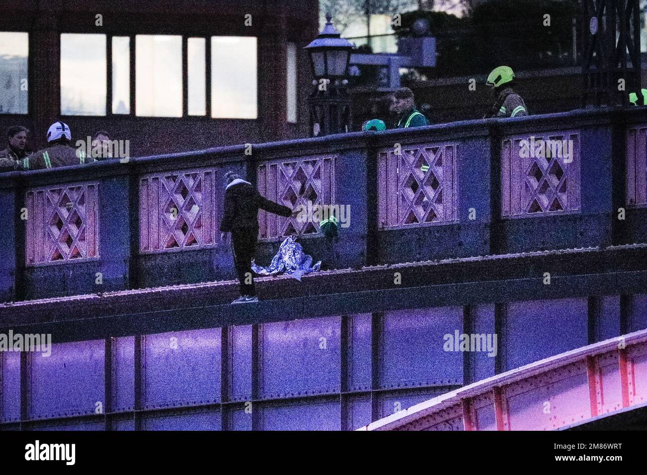 London, UK. 12th Jan, 2023. The woman can be seen suddenly standing up on the outer ledge of the bridge, with a large presence of paramedics, rescue service workers, police and others in attendance on the bridge behind, as well as on the River Thames. Lambeth Bridge in Westminster was closed for several hours this afternoon and evening as a woman had climbed over the railings, with possible intentions of jumping into the river. Whilst police rescue services were patrolling the river, freight and some passenger boats were still passing underneath. Credit: Imageplotter/Alamy Live News Stock Photo