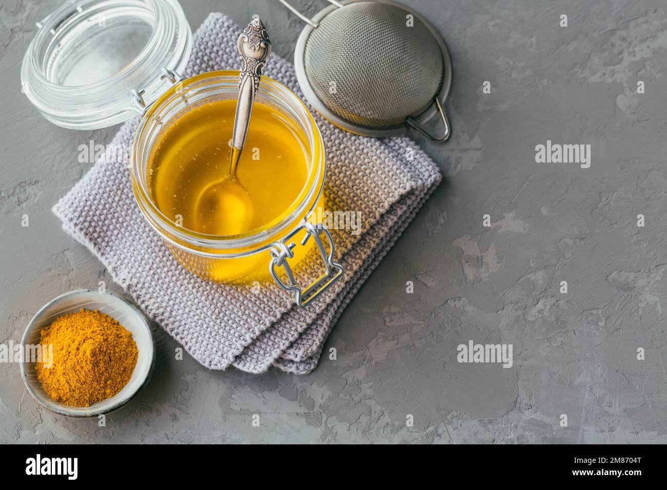 Homemade Ghee or clarified butter in a jar and turmeric powder on grey