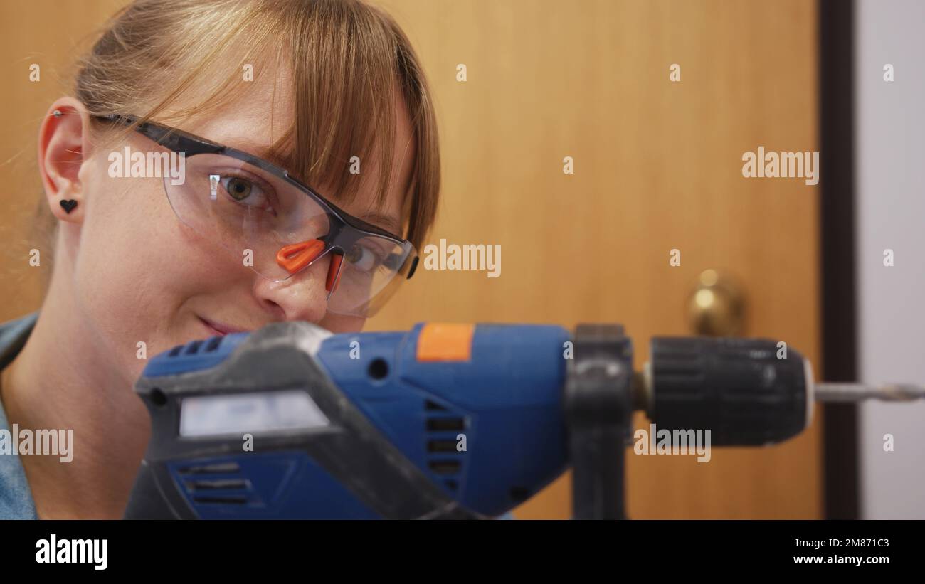 closeuo view of a woman with safety glasses using a drill into a wall, repair concept. High quality photo Stock Photo