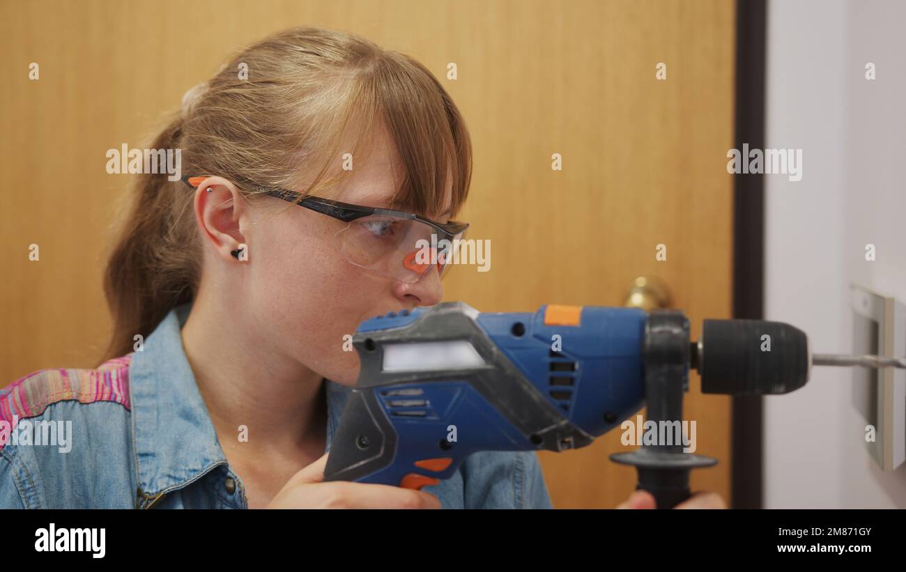 Caucasian woman wearing safety glasses and using a drill at home, independent woman. High quality photo Stock Photo