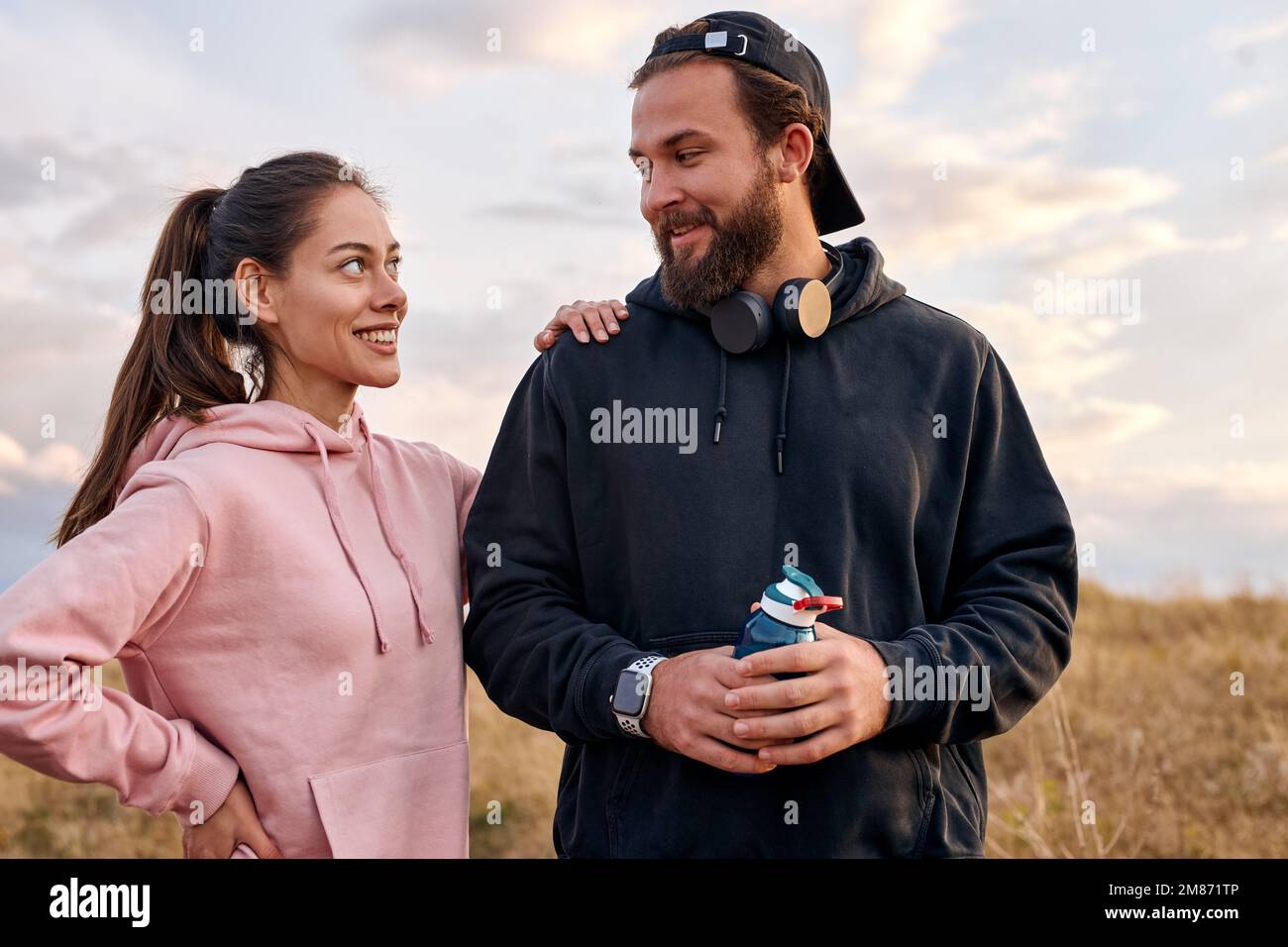 Outdoor portrait of excited couple in nature countryside relaxing before or after jogging. beautiful woman and man in hoodie laughing, talking. wellbe Stock Photo