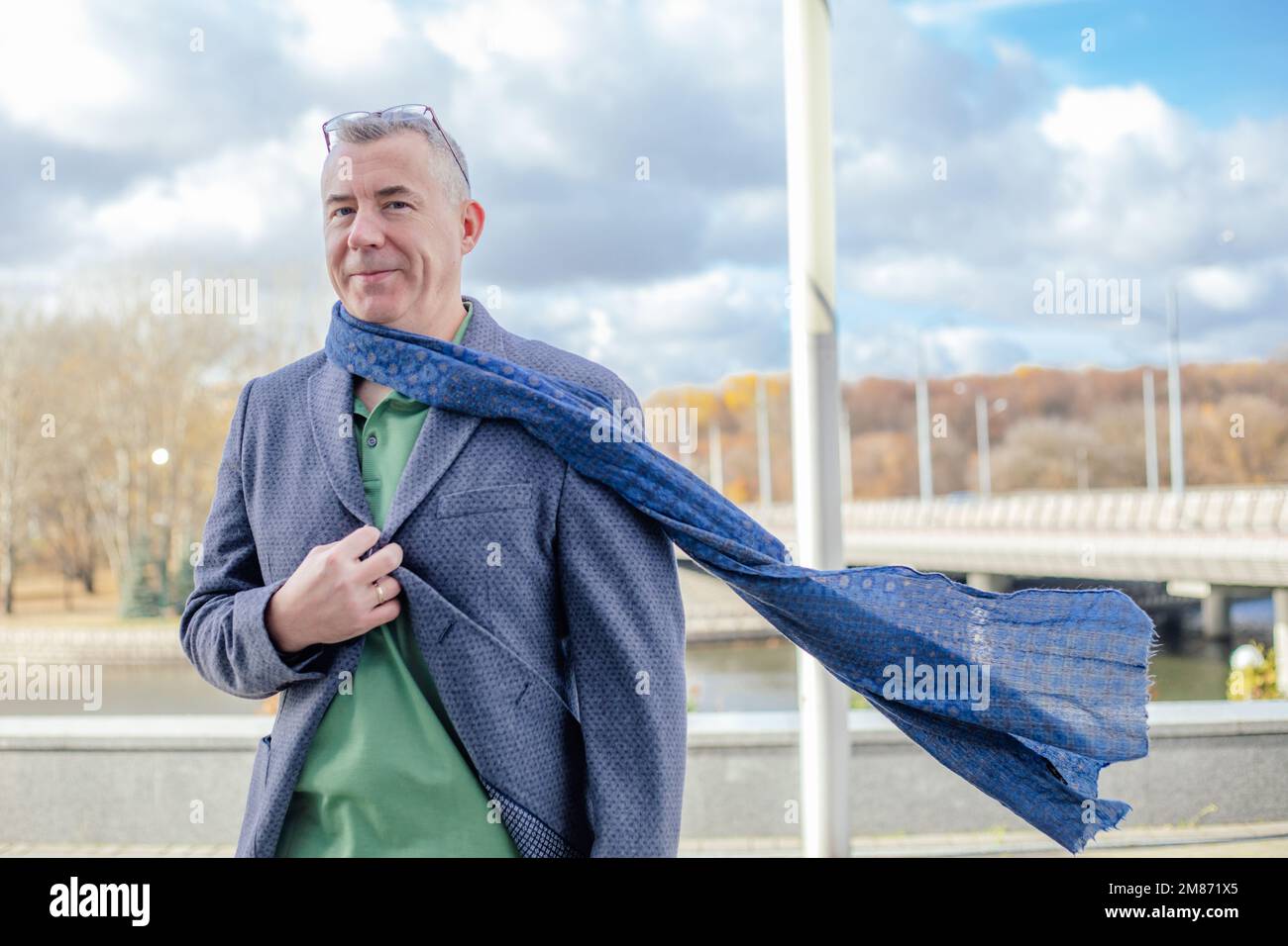 Satisfied, confident, smiling grizzled businessman with eyeglasses on head in warm jacket, scarf walk, shiver on street Stock Photo