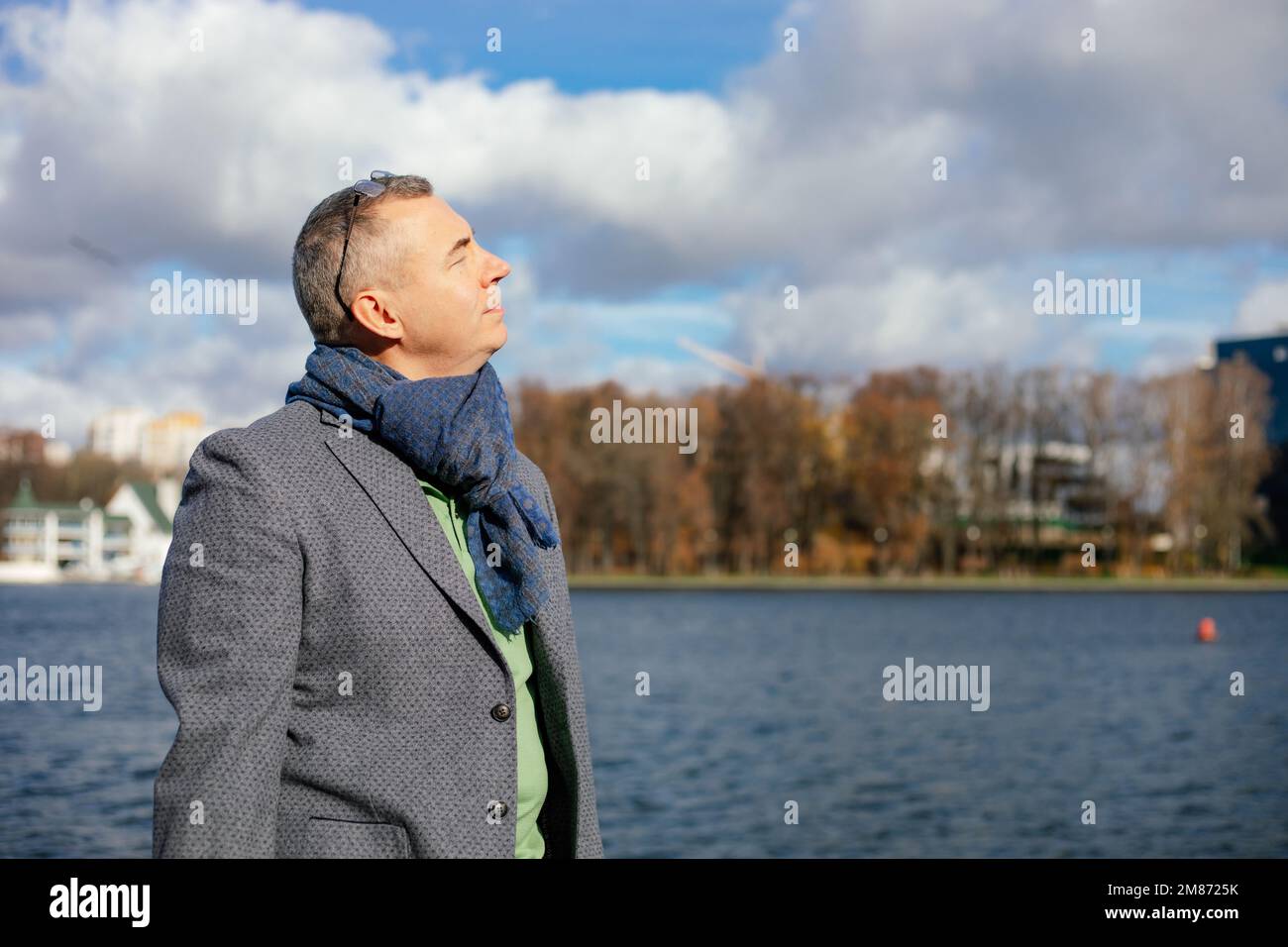 Close up grizzled mature retire man with eyeglasses on head in jacket and scarf stand near river and breath fresh air Stock Photo