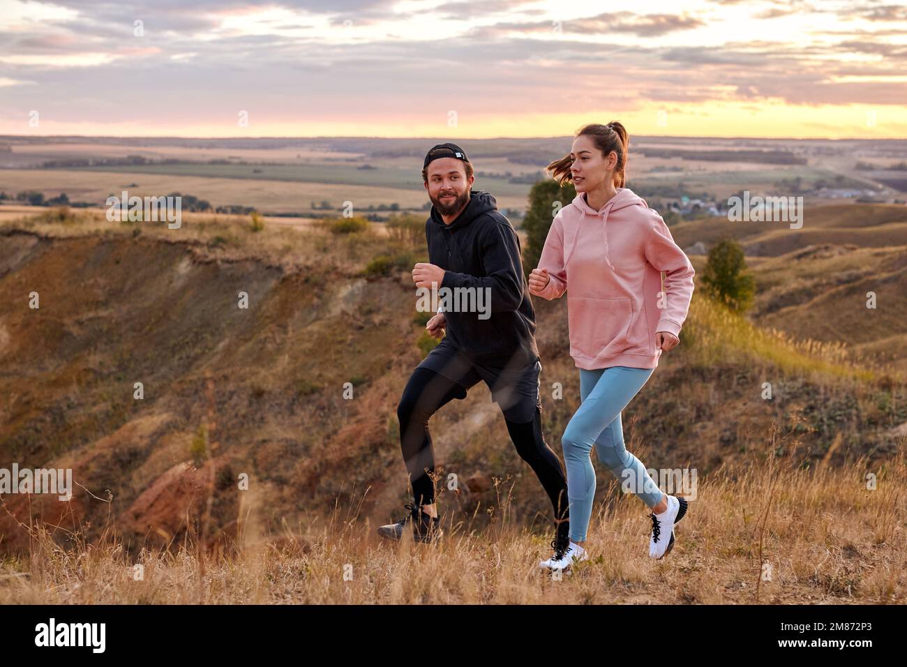 couple running at sunset or sunrise along field mountains, morning ...