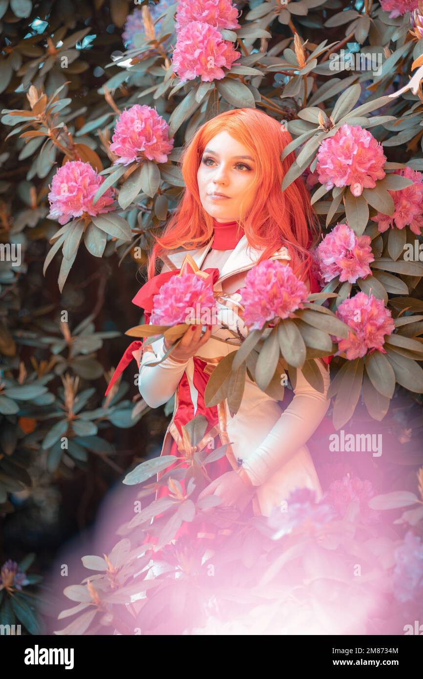 A vertical shot of a Caucasian female in miss fortune cosplay costume standing in front of flowers Stock Photo