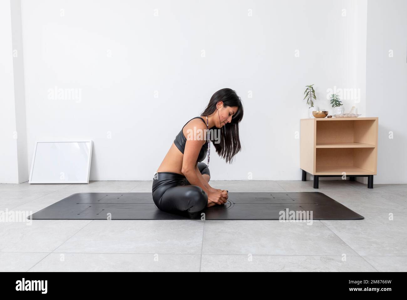 Young Hispanic woman, doing the Bound Angle pose, in a yoga studio, wearing sportswear. Stock Photo