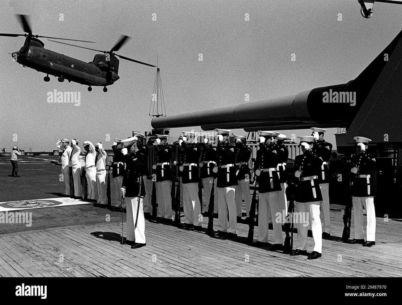 Members of a Marine honor guard and side boys hold onto their hats as a U.S. Army CH-47 Chinook helicopter takes off from the deck of the battleship USS IOWA (BB-61). The helicoptger is being used for personnel transport and re-supply while the ship is in port to participate in a civic action program. Base: Puerto Cortes Country: Honduras (HND) Stock Photo
