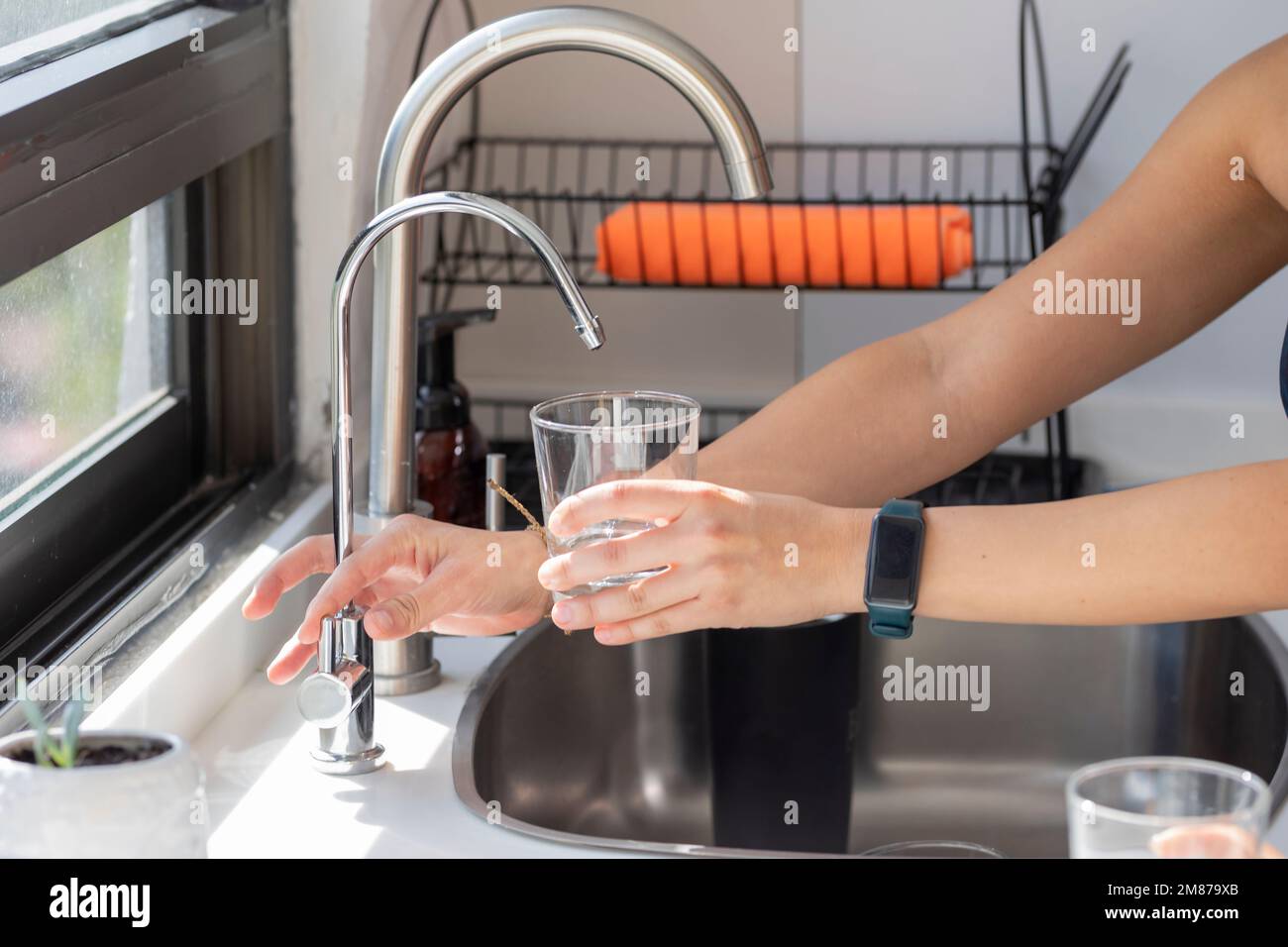 Woman's hands holding a glass that fills with water from the tap filter. Stock Photo