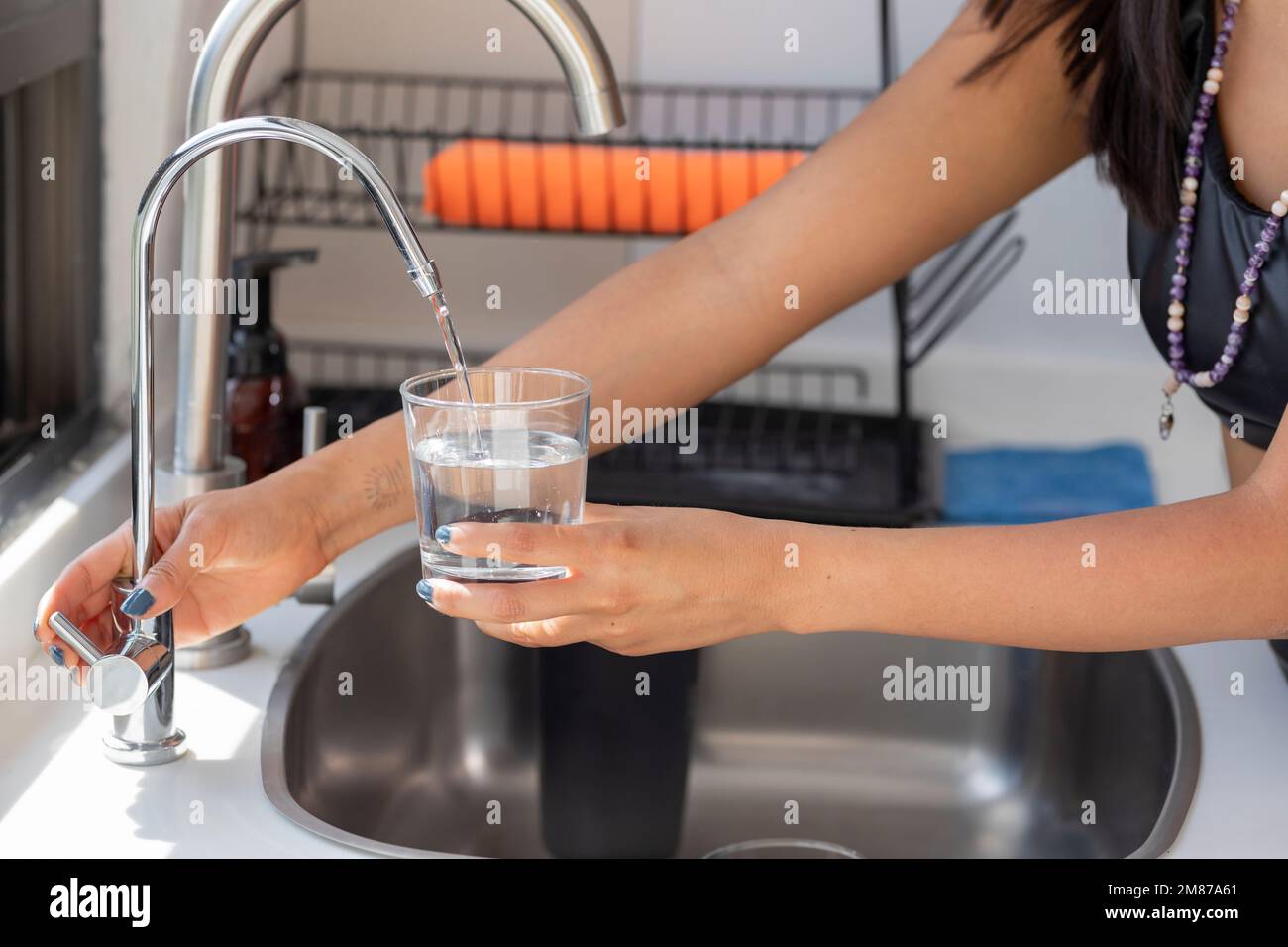 Woman's hands holding a glass that fills with water from the tap filter. Stock Photo