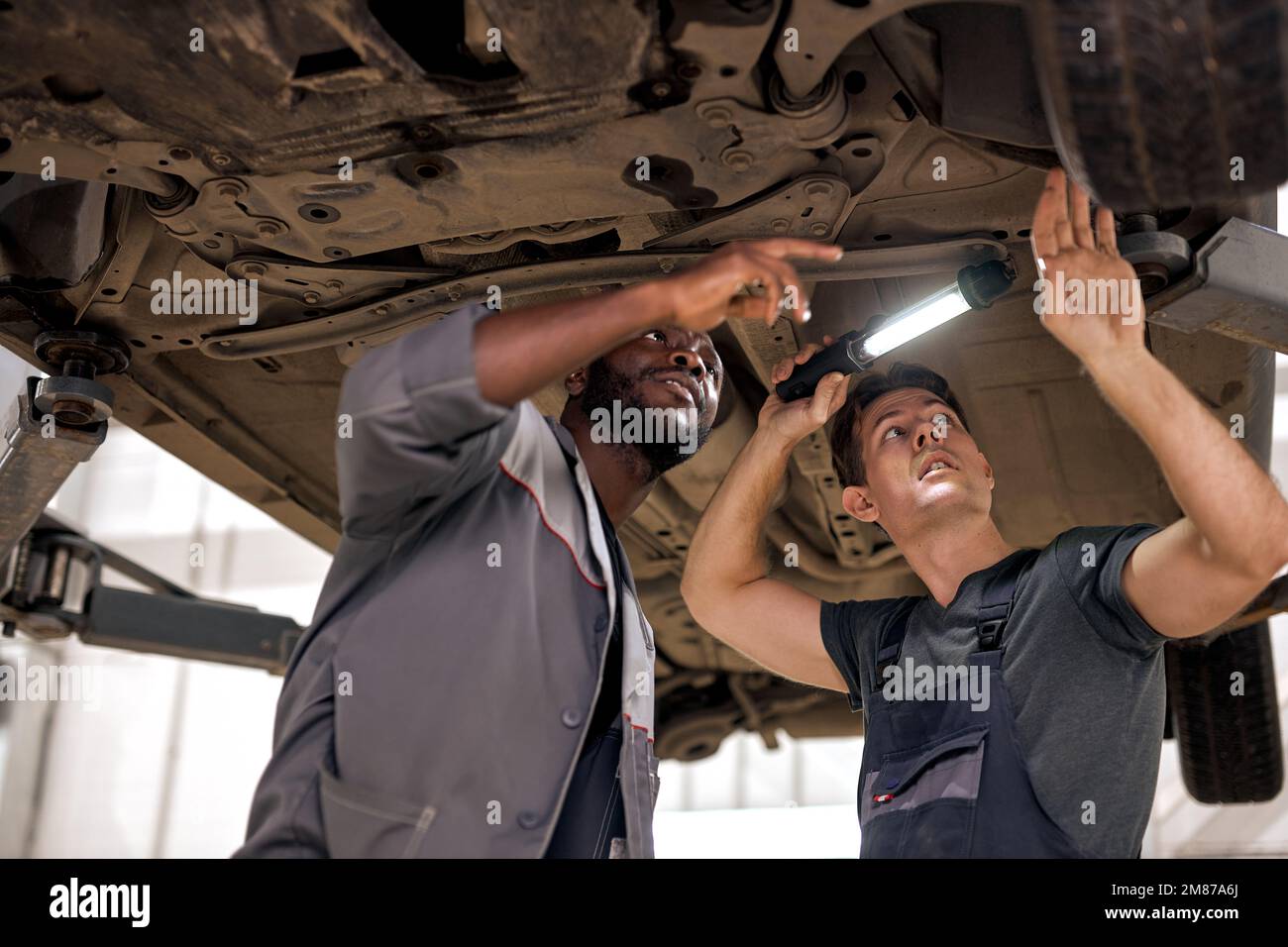 Two young auto mechanics working on undercarriage of car diligence