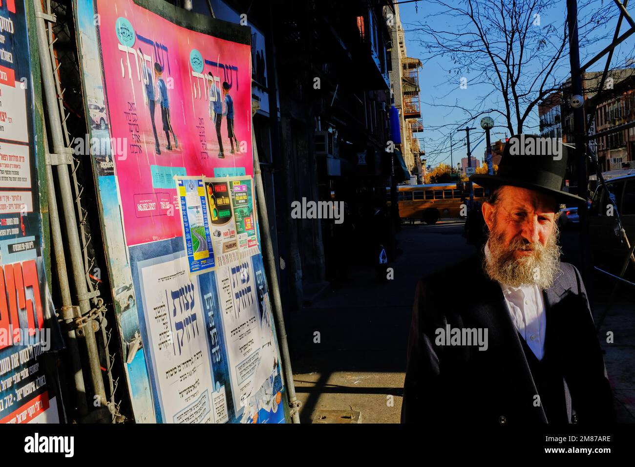 An old Orthodox Jewish man walking by posters in Yiddish along Lee