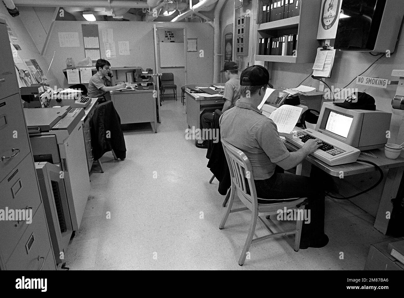 Crew members process paperwork in the supply department office aboard