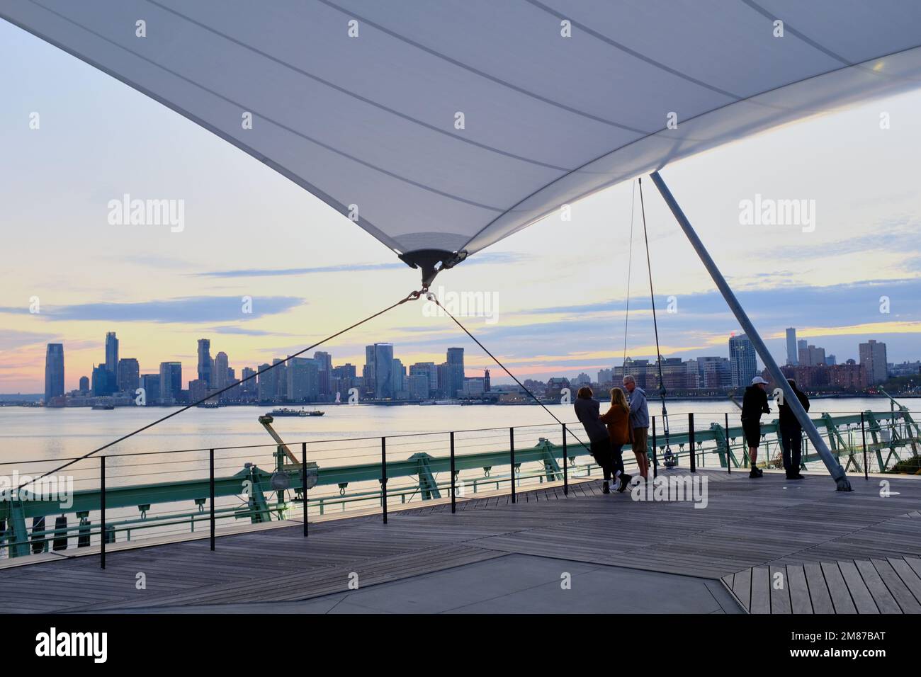 Visitors at Pier 57 Rooftop Park with Hudson River and Jersey City skyline in the background after sunset.Manhattan.New York City.USA Stock Photo