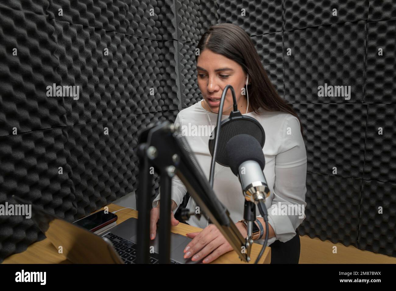 Woman speaking into a microphone in an audio booth, while recording a podcast. Stock Photo