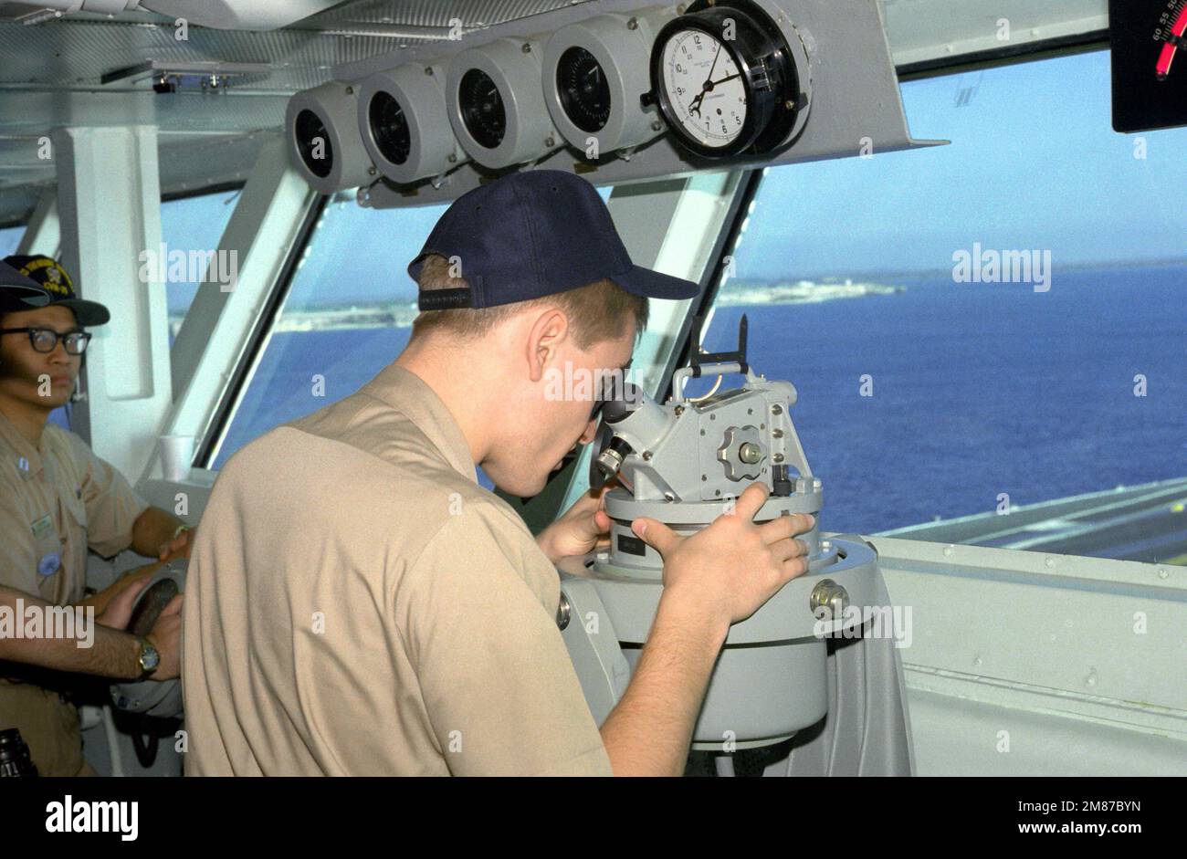A sailor uses a telescopic alidade to take a bearing from the bridge of the nuclear-powered aircraft carrier USS THEODORE ROOSEVELT (CVN-71). Country: Unknown Stock Photo